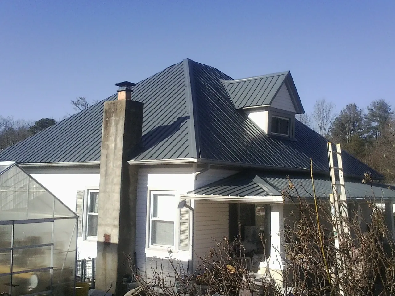 Dark blue standing seam metal roof on a white farmhouse with dormer — Slate & Tile Roof Repair by Roofing Brothers in Milroy