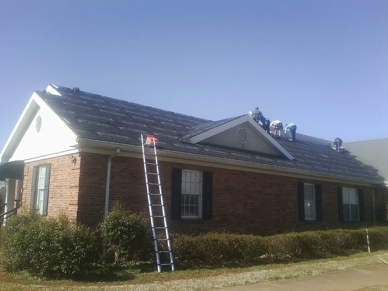 Crew tearing shingles off a brick ranch roof with a ladder set — Emergency Roof Repair work by our crew in Milroy