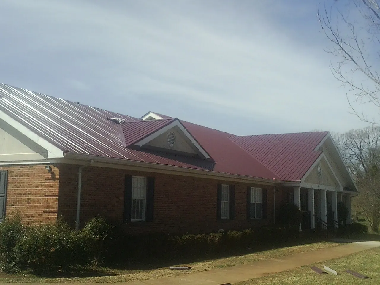 Red metal roof with gabled entries on a long brick building, from a Hail Damage Roof Repair job in Milroy