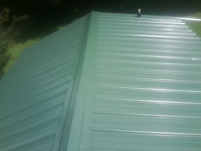 New green metal panels meeting at the ridge of a roof — Flat Roof Repair work by our crew in Milroy