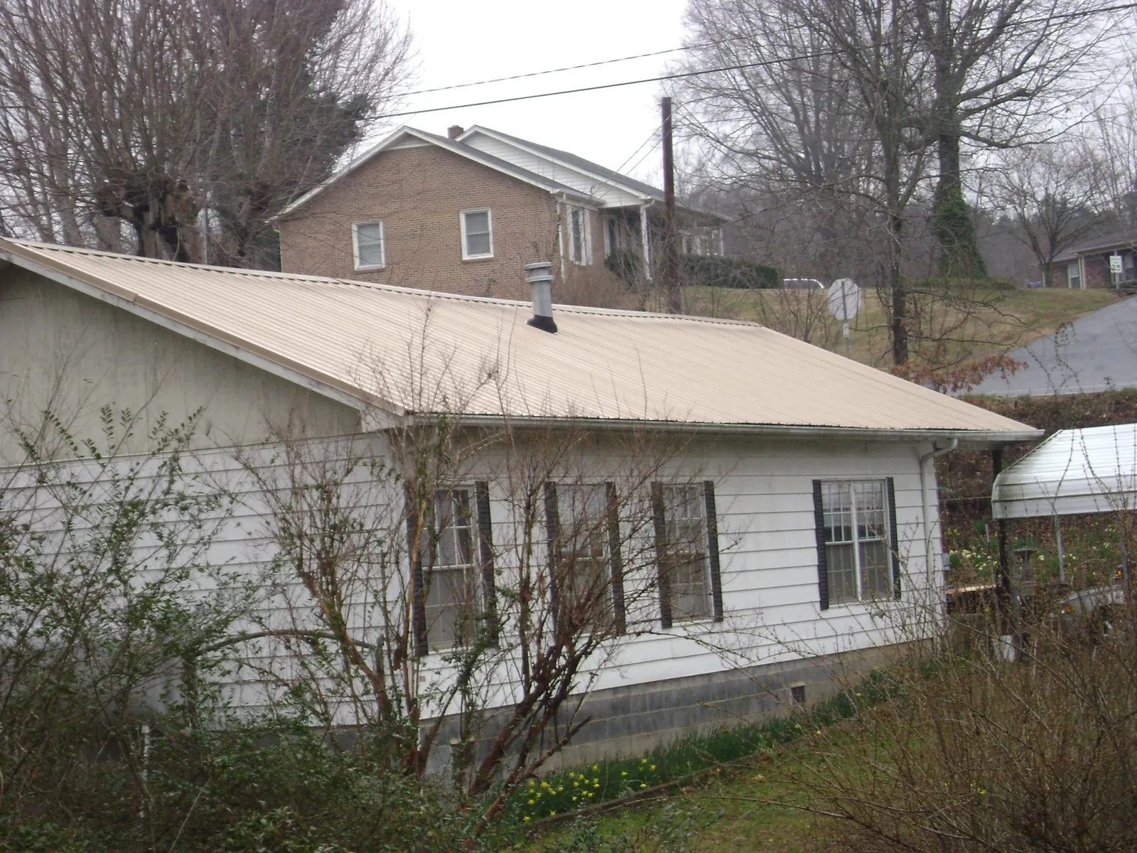 Tan metal roof on a white sided house set into a hillside — Commercial Roofing by Roofing Brothers in Milroy